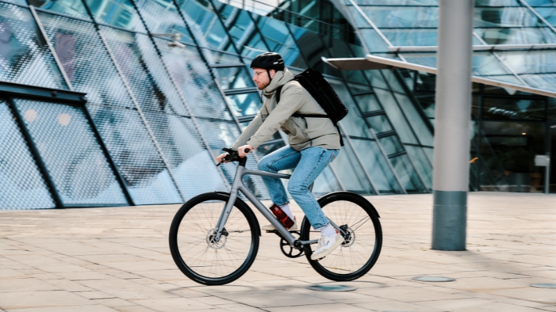Man with backpack commuting with bike through city 