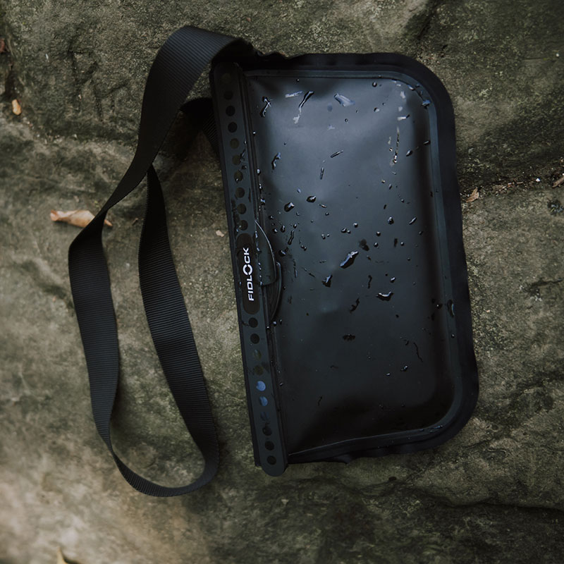 FIDLOCK-HERMETIC-sling-bag-schwarz-outdoor-auf-einem-Stein-liegend