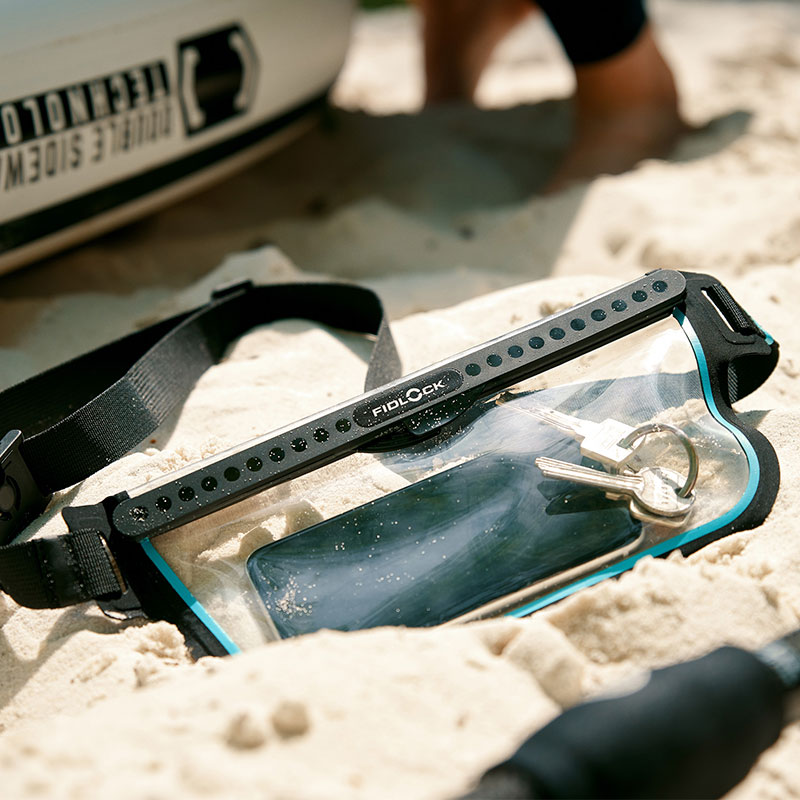 FIDLOCK-HERMETIC-sling-bag-transparent-outdoor-liegt-im-sand-gefüllt